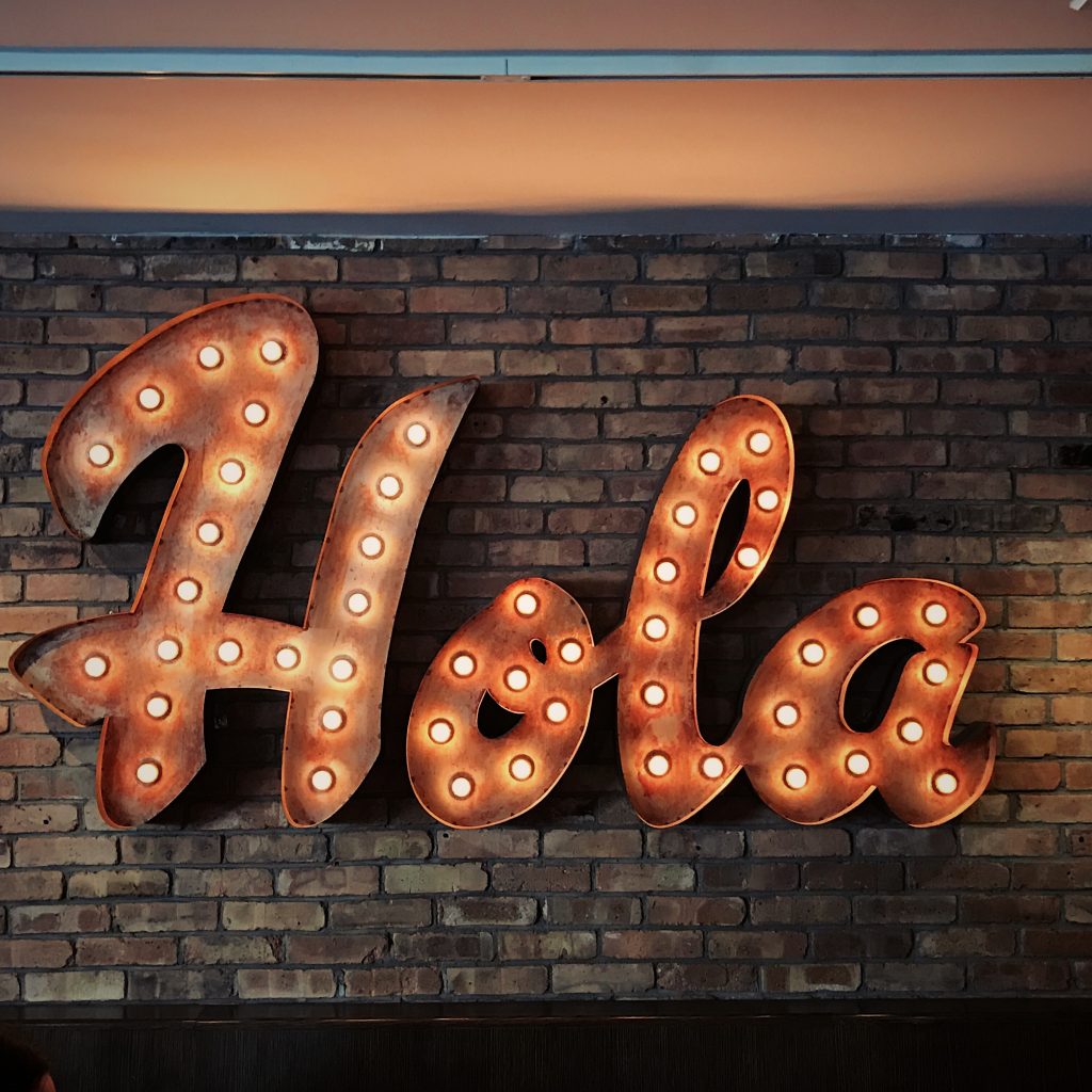 "Hola" written in lights on a brick wall.